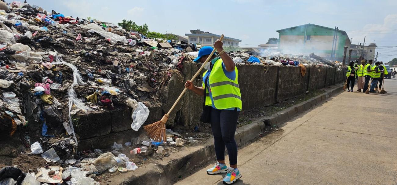 Women with broom sweeping near a pile of trash